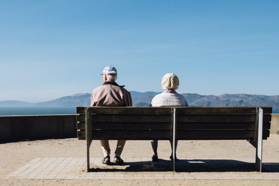 An elderly man and woman sitting on a park bench looking at a body of water.